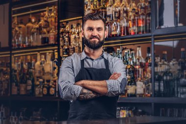 Bir gömlek ve önlük ayakta bar counter arka plan çapraz kollu şık acımasız barmen.