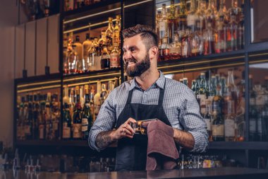 Neşeli şık acımasız barmen bir bezle bar counter arka plan cam temizlik.