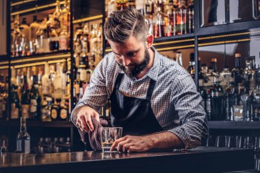 Bir gömlek ve önlük şık acımasız barmen, bir kokteyl bar counter arka plan yapar.