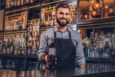 Neşeli şık acımasız barmen bir gömlek ve önlük özel alkol counter arka plan bir şişe sunar.