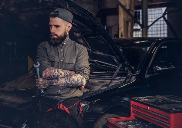 ひげを生やしたオート メカニック交差自動車修理工場で車に対して立っている間手 — ストック写真