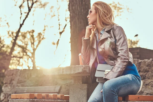 时髦的金发女郎放松户外 坐在城市公园的长凳上 对明亮的阳光 — 图库照片