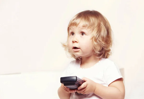 Portret van een schattig klein meisje in een witte jurk houdt een tv remote op witte achtergrond. — Stockfoto