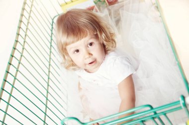 Beyaz arka plan üzerinde alışveriş arabası oturan beyaz bir elbise, sevimli küçük bir kız portresi.