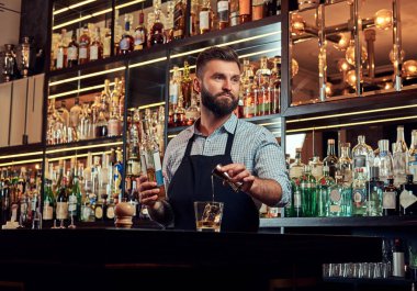 Bir gömlek ve önlük şık acımasız barmen, bir kokteyl bar counter arka plan yapar.