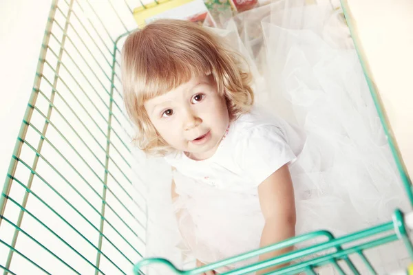 Porträt eines niedlichen kleinen Mädchens in einem weißen Kleid, das in einem Einkaufswagen mit weißem Hintergrund sitzt. — Stockfoto