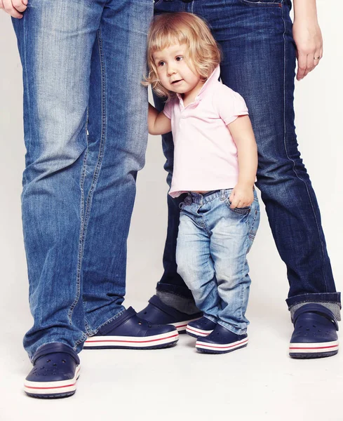 Portret van een schattig klein meisje in shirt en spijkerbroek permanent met haar ouders op witte achtergrond. — Stockfoto