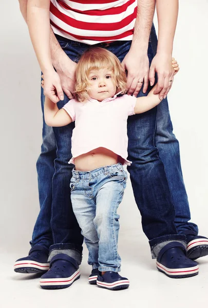 Portret van een schattig klein meisje in shirt en spijkerbroek permanent met haar ouders op witte achtergrond. — Stockfoto