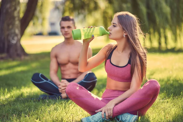 Healthy lifestyle concept. Happy young fitness couple sitting in lotus pose on a green grass. — Stock Photo, Image