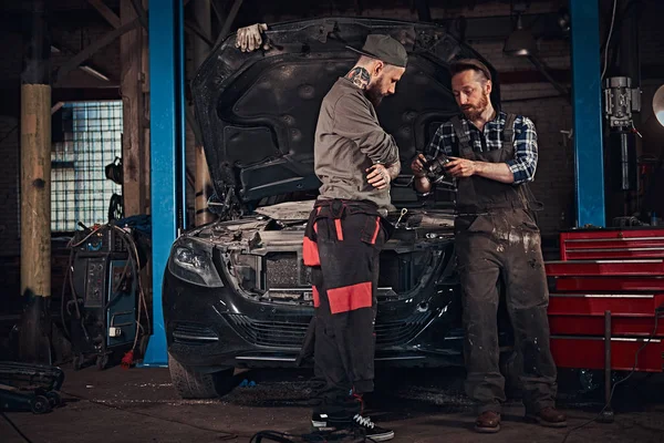 Deux mécaniciens parlent pendant les réparations d'une voiture cassée dans un garage . — Photo