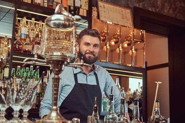Stylový vousatý barman v košili a zástěra stojí u baru counter pozadí. — Stock fotografie