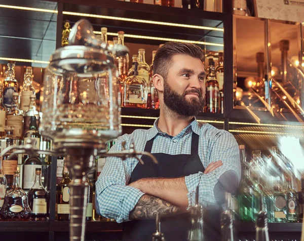 Bartender brutal bergaya dalam kemeja dan celemek berdiri dengan lengan silang di latar belakang bar counter . — Stok Foto