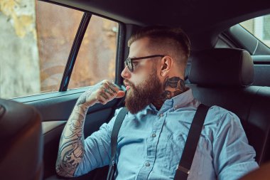 Lüks bir araba bir arka koltukta oturan askısı ile bir gömlek dalgın eski moda dövmeli hipster adam uzağa arıyorsunuz.