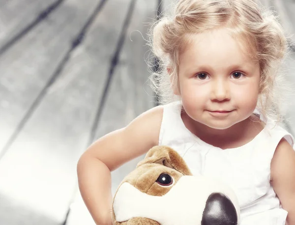 Retrato de uma menina bonita em vestido casual sentado com um brinquedo de pelúcia em estúdio . — Fotografia de Stock