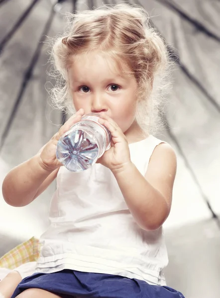 Porträt eines lustigen netten kleinen Mädchens in einem lässigen Kleid, das im Studio Wasser trinkt. — Stockfoto