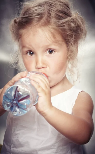 Porträt eines lustigen netten kleinen Mädchens in einem lässigen Kleid, das im Studio Wasser trinkt. — Stockfoto