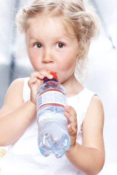 Porträtt av en rolig söt liten flicka i en casual klänning, Drick vatten när du sitter i studio. — Stockfoto