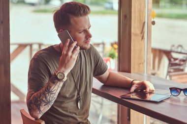Yakışıklı şık hipster Smartphone'da söz yol kenarına yerleştirilen bir kafede bir masada oturur.