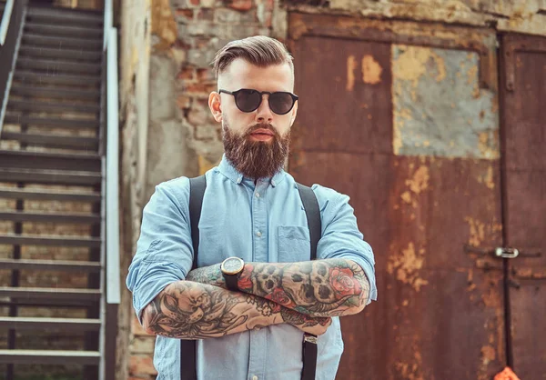 Стильний красивий старомодний татуйований хіпстер у сорочці з підтяжками, що стоїть біля старої будівлі на відкритому повітрі . — стокове фото