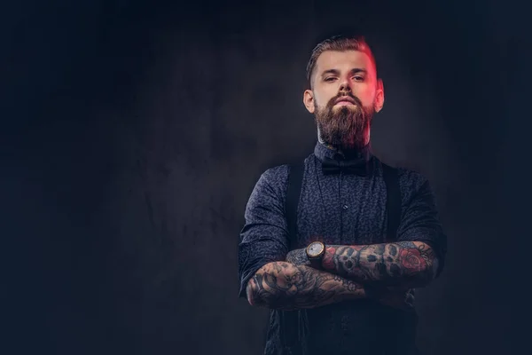 Retrato de um belo hipster à moda antiga com uma camisa azul e suspensórios, de pé com os braços cruzados em um estúdio . — Fotografia de Stock