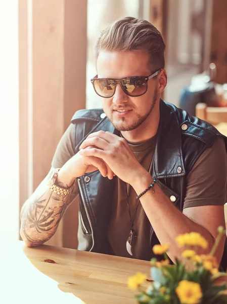 Hipster con un taglio di capelli elegante e la barba si siede a un tavolo in un caffè lungo la strada . — Foto Stock