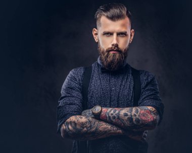 Mavi bir gömlek ve bir stüdyo çapraz kollarında ile ayakta pantolon askısı, yakışıklı bir eski moda hipster portresi.