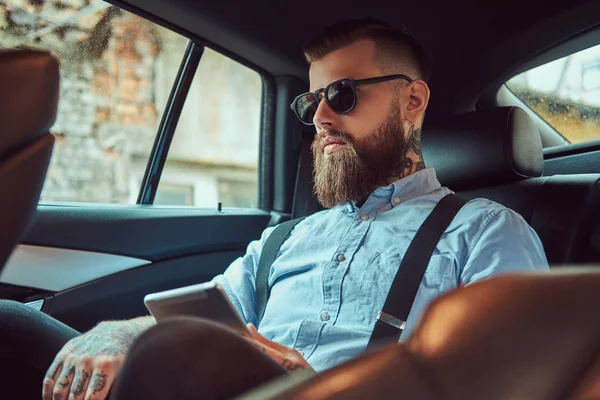 Staromódní Tetovaný bokovky chlap v košili s podvazky sedí v autě na zadním sedadle luxusní. — Stock fotografie