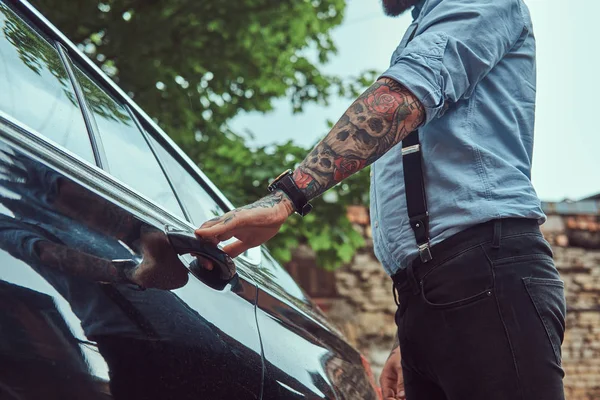 Cropped image of an old-fashioned tattooed man in a shirt with suspenders, who is going to get into a car.