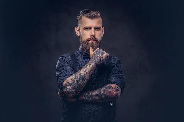 Pensif beau hipster à l'ancienne dans une chemise bleue et des bretelles, debout avec la main sur le menton dans un studio . — Photo