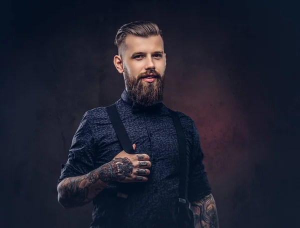 Sonriente guapo hipster a la antigua con una camisa azul y tirantes, posando en un estudio . — Foto de Stock