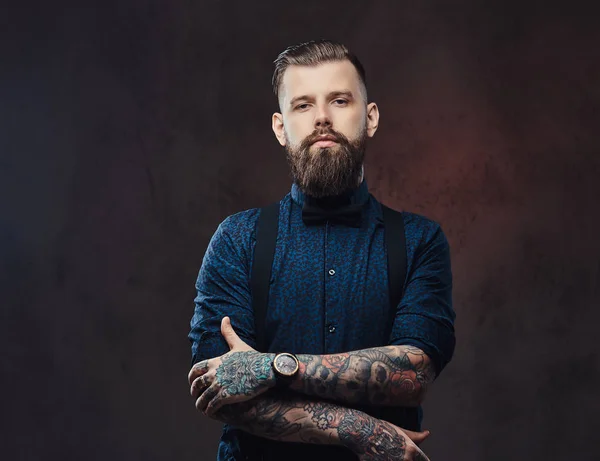 Retrato de um belo hipster à moda antiga com uma camisa azul e suspensórios, de pé com os braços cruzados em um estúdio . — Fotografia de Stock