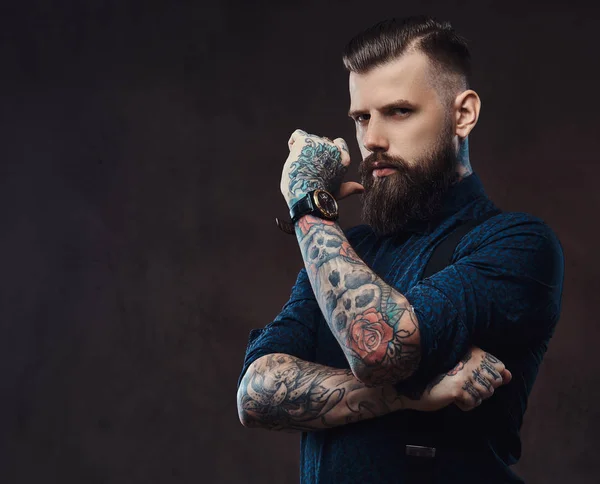 Pensativo guapo hipster anticuado en una camisa azul y tirantes, de pie con la mano en la barbilla en un estudio . —  Fotos de Stock