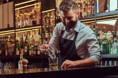 Buz bir kokteyl bar counter arka plan yapmak için bir gömlek ve önlük şık sakallı barmen böler.