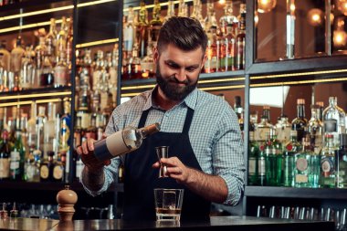 Bir gömlek ve önlük şık acımasız barmen, bir kokteyl bar counter arka plan yapar.