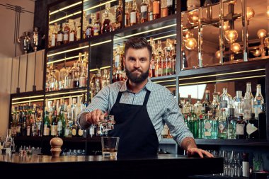 Bir gömlek ve önlük şık acımasız barmen, bir kokteyl bar counter arka plan yapar.