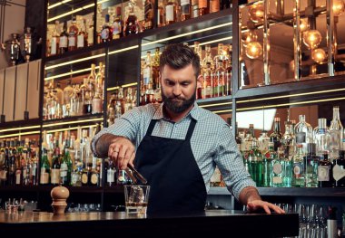 Bir gömlek ve önlük şık acımasız barmen, bir kokteyl bar counter arka plan yapar.