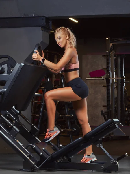 Athletic Blondynka w pozowanie w pobliżu maszyny prasy nogi w siłowni sportowej. — Zdjęcie stockowe