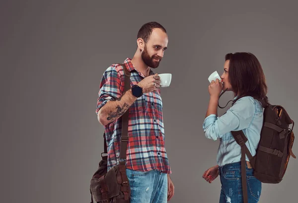 Feliz pareja de turistas, toma tazas de café, se paran en el estudio mirándose . — Foto de Stock