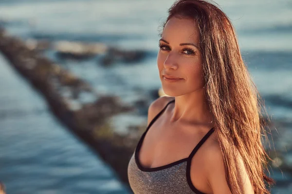 Schöne Fitness-Frau in grauer Sportbekleidung posiert vor einem Meereshintergrund. — Stockfoto