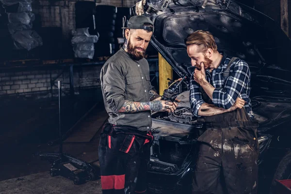 Dwóch mechaników mówi podczas naprawy uszkodzonego samochodu w garażu. — Zdjęcie stockowe