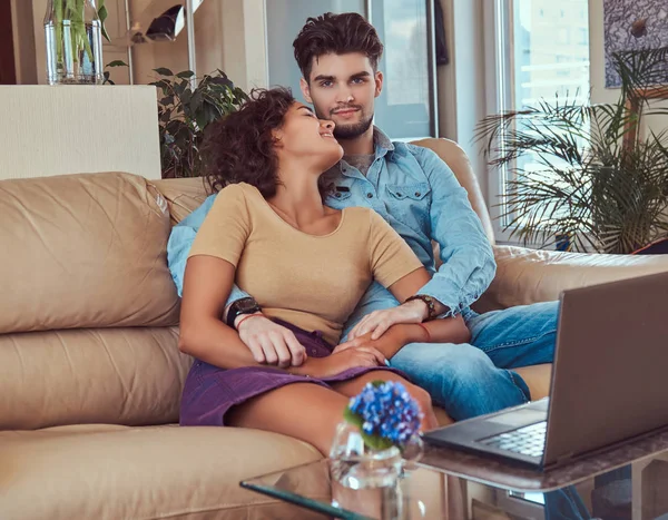 Feliz casal atraente durante um fim de semana, assistindo filme no laptop sentado no sofá em casa . — Fotografia de Stock