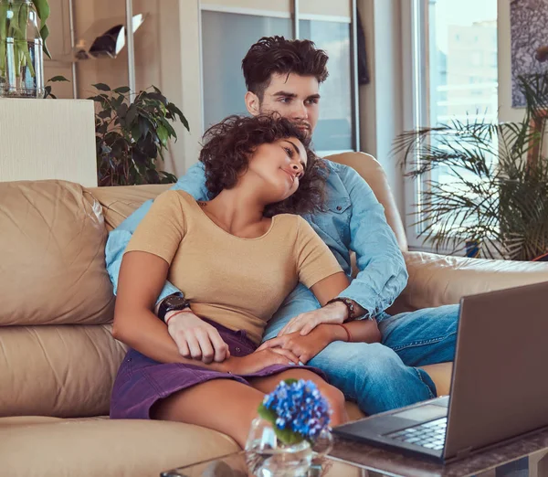 Feliz casal atraente durante um fim de semana, assistindo filme no laptop sentado no sofá em casa . — Fotografia de Stock