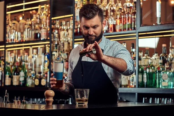Stylový brutální barman v košili a zástěra je koktejl v baru counter pozadí. — Stock fotografie