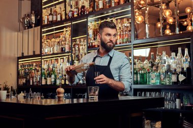 Bir gömlek ve önlük şık acımasız barmen, bir kokteyl bar counter arka plan yapar.