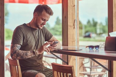 Çıkıyor Smartphone yakışıklı şık hipster yol kenarına yerleştirilen bir kafede bir masada oturur.