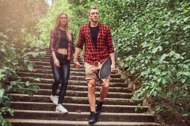 Genç hippi çift, elele, merdivenlerden inen bir parkta yürümek.