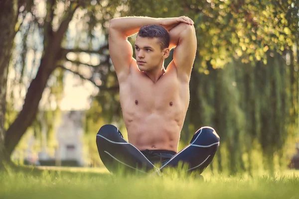 Concept de mode de vie sain. Jeune homme torse nu étirant les mains tout en étant assis dans la pose du lotus sur une herbe verte . — Photo