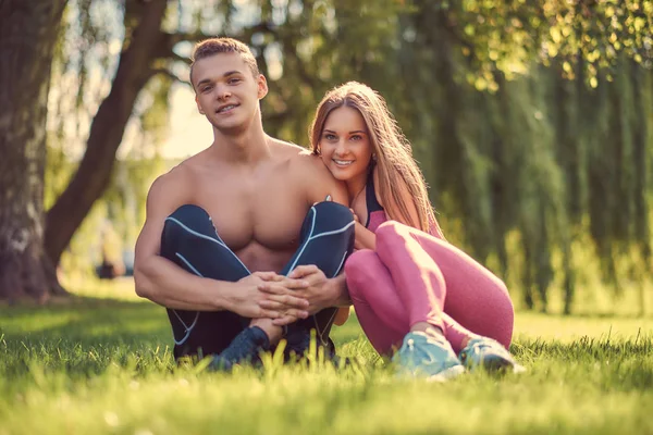 Concepto de estilo de vida saludable. Feliz pareja de fitness joven abrazándose mientras está sentado en la hierba verde . —  Fotos de Stock