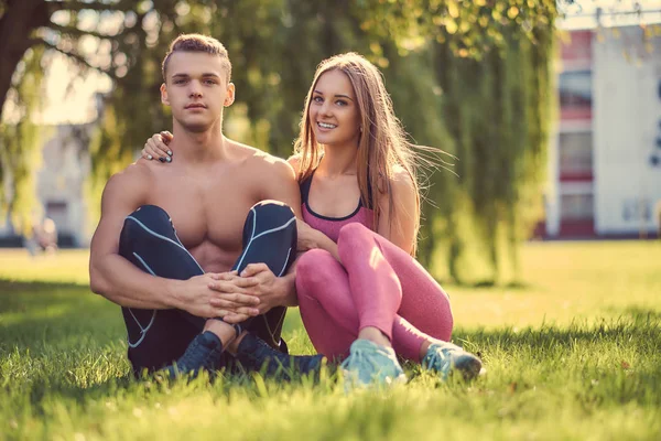 Здоровий спосіб життя. Щаслива молода фітнес-пара надувається, сидячи на зеленій траві . — стокове фото