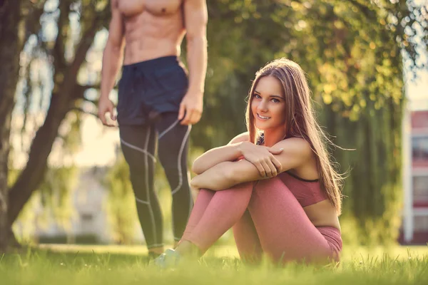 Egészséges életmód fogalma. Boldog fiatal fitness pár hozzábújva ülve, a zöld fű. — Stock Fotó